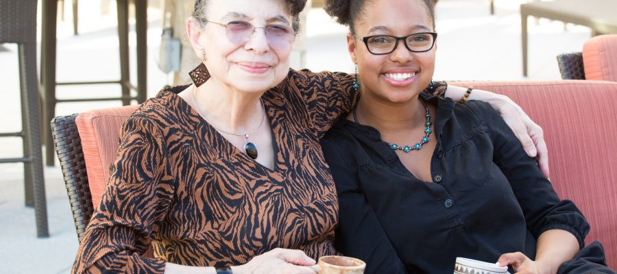 Closeup portrait, granddaughter and grandmother sitting, enjoying drinks coffee and tea together, isolated outdoors background